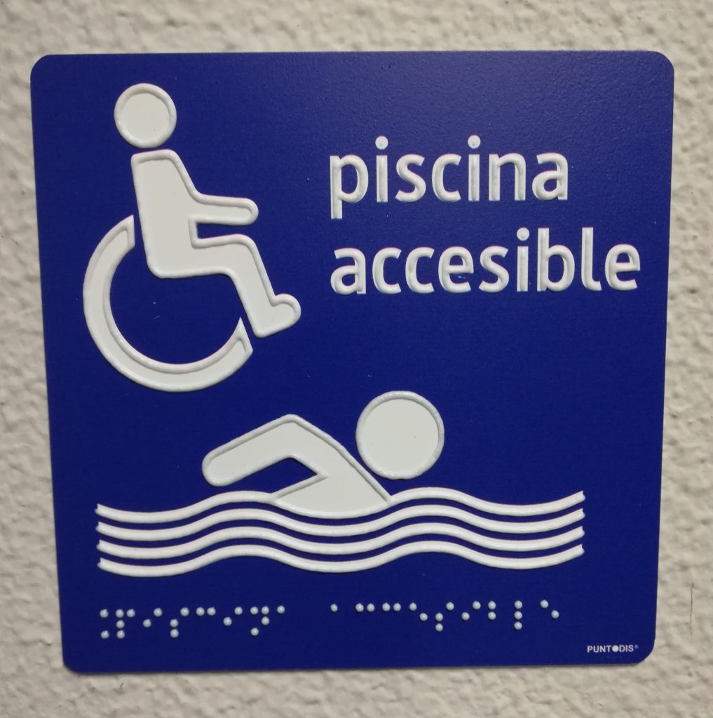 Señal piscina accesible en fondo azúl, pictogramas y braille en blanco